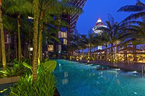 A pool area with palm trees, a building with a dome-shaped structure, and a well-lit walkway. - Crowne Plaza Changi Airport by IHG (Singapore)