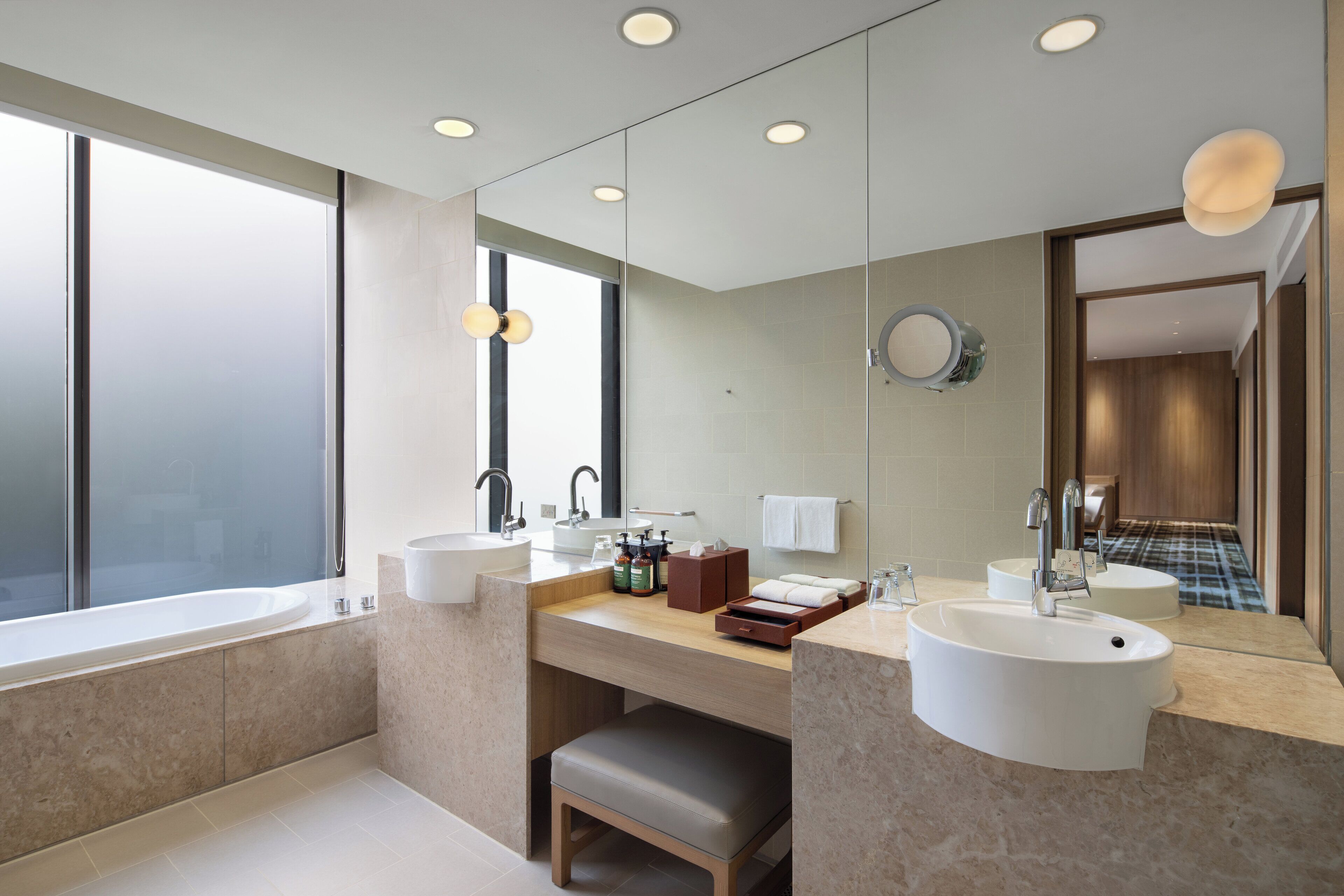 Un baño moderno con una bañera grande, dos lavamanos, un tocador con espejo y un banco.