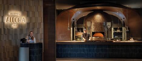 A restaurant interior with a modern design, a bar area, and a visible kitchen with a brick oven.