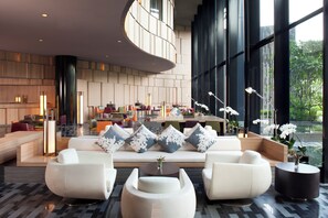 A modern lobby with a curved ceiling, a seating area with sofas and armchairs, and a dining space with round tables and chairs.