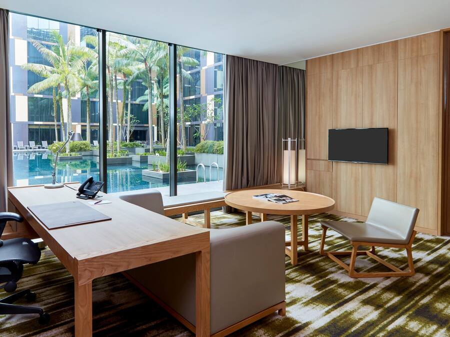 A hotel room with a large window, a desk with a chair, a round table with a chair, a bed, and a TV on the wall.