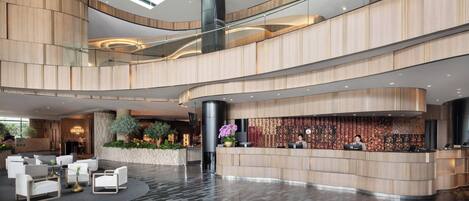 A spacious lobby with a curved reception desk, seating area, and a high ceiling with skylights.