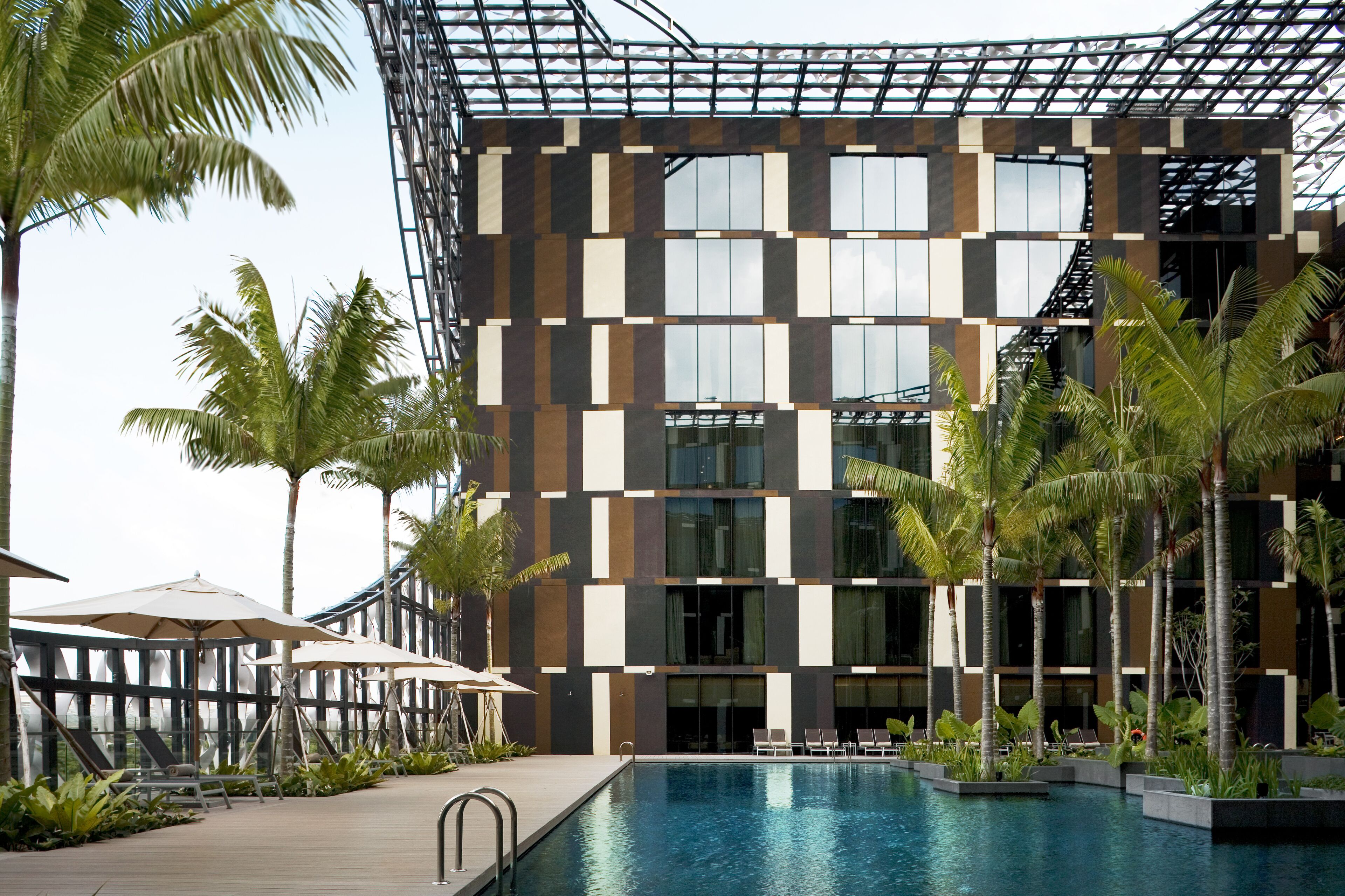 A modern hotel with a pool area, palm trees, and outdoor seating.