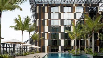 A modern hotel with a pool area, palm trees, and outdoor seating.