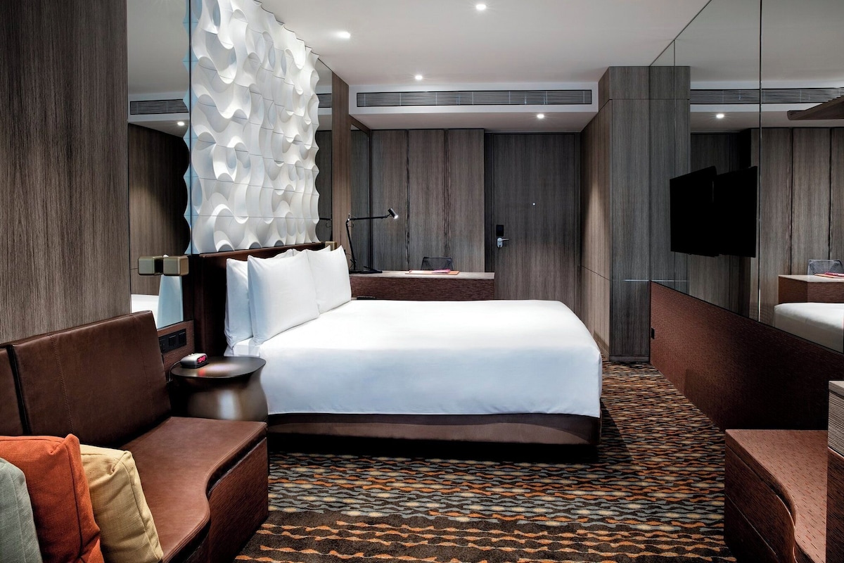 A modern hotel room with a large bed, a sofa, a desk, and a TV.
