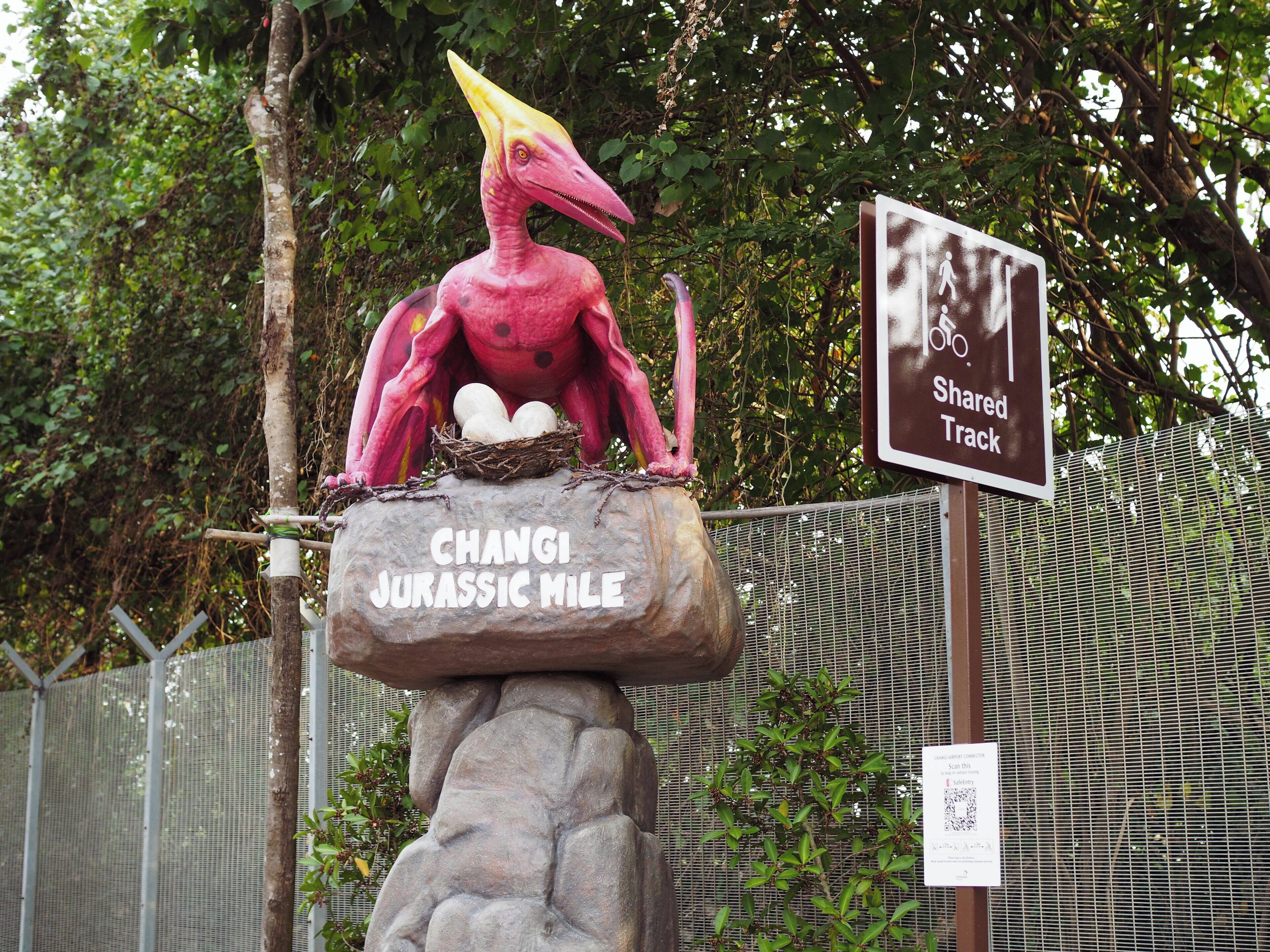 A dinosaur statue on a rock with a sign indicating a shared track.