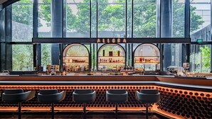 Un bar con una estantería para vinos, tres taburetes y un ventanal con vistas a árboles.