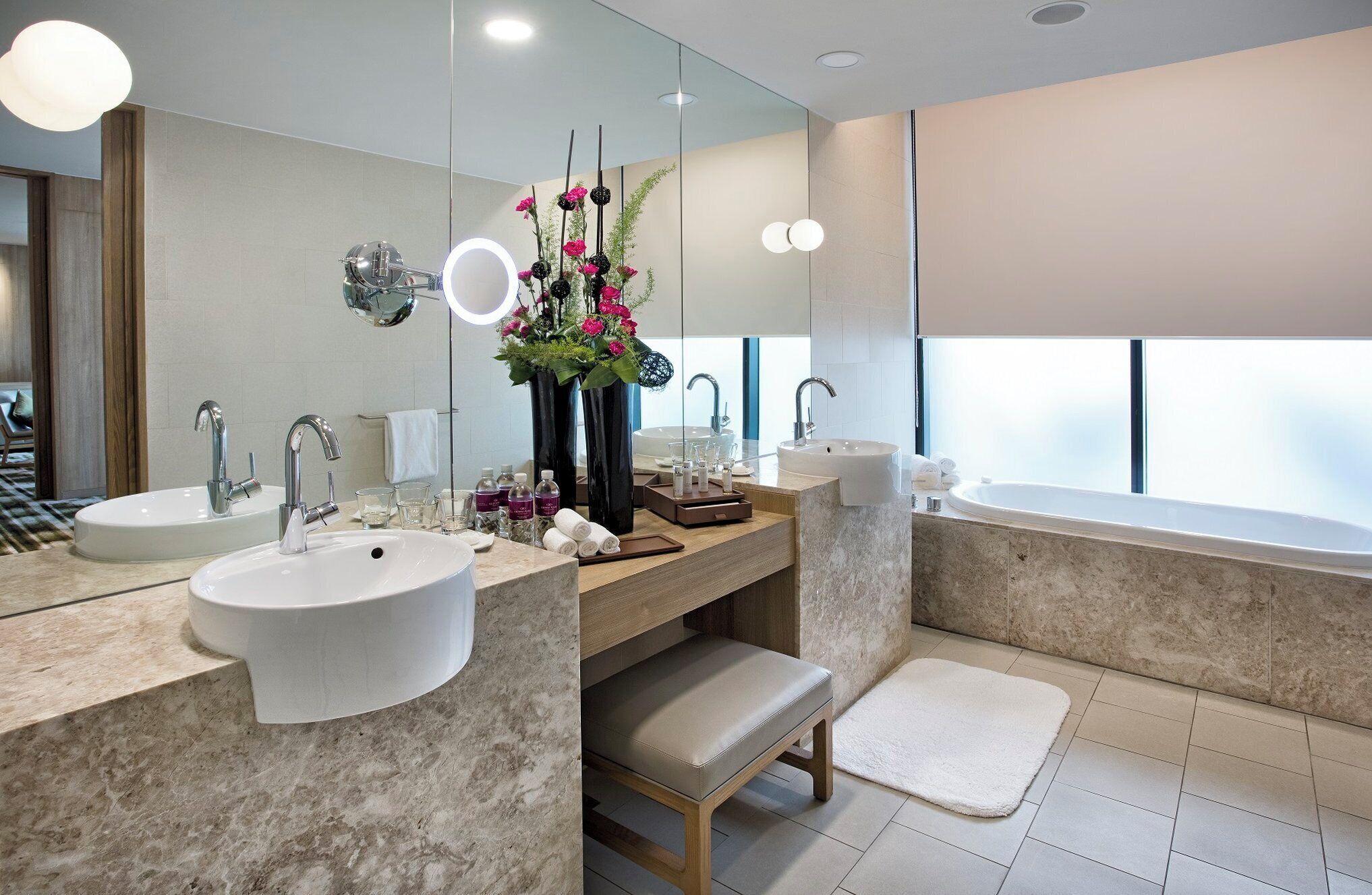A modern bathroom with two sinks, a large mirror, a vanity, a bathtub, and a window.