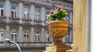 A balcony with a wrought iron balustrade, a large decorative urn with flowers, and a classical building with ornate windows in the background. - EA Hotel Downtown (Prague)