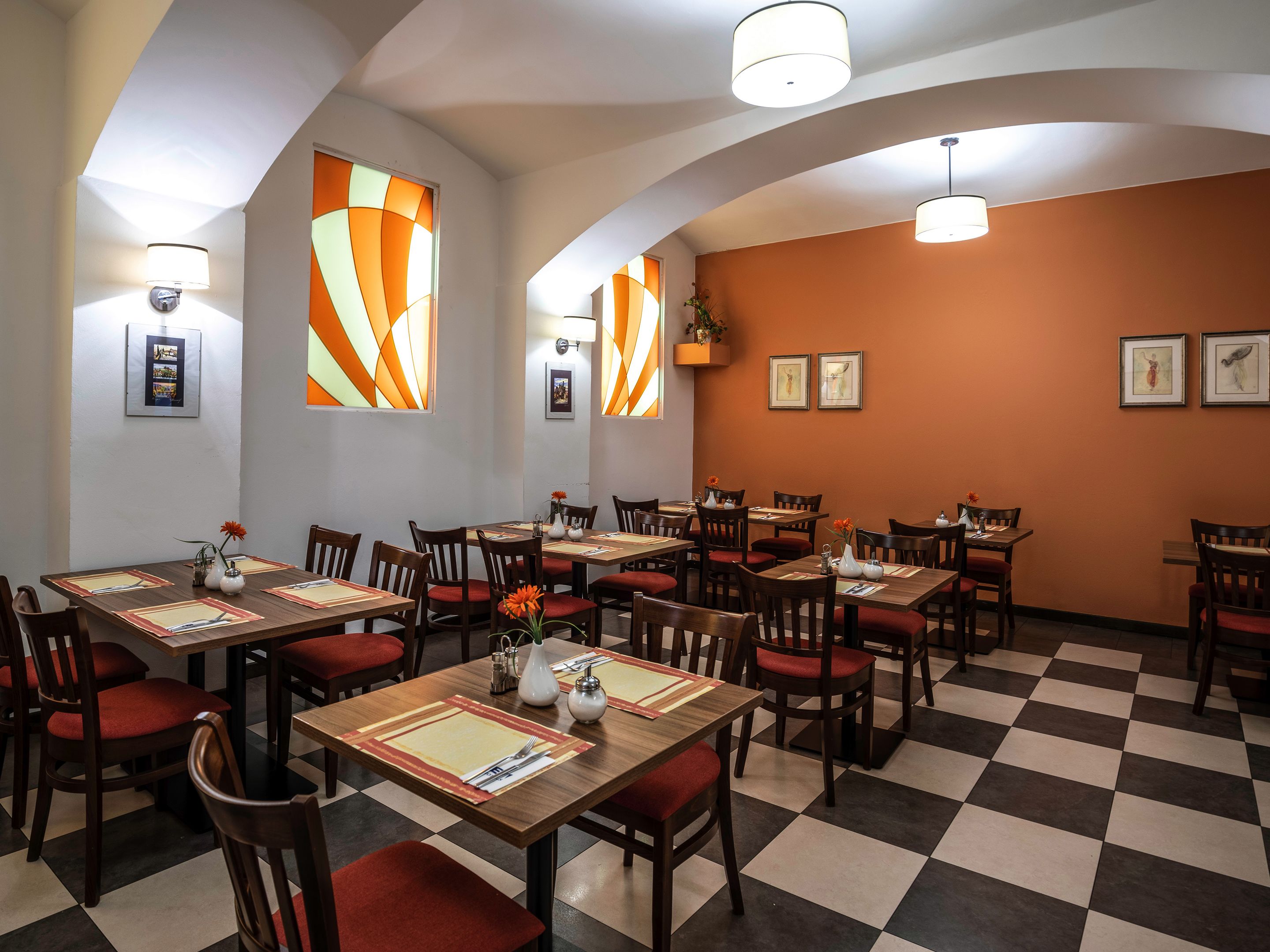 A restaurant with a checkered floor, wooden tables, and red cushioned chairs.
