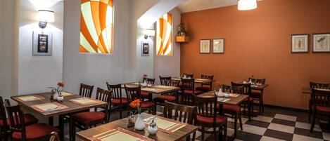 Um restaurante com chão quadriculado, mesas de madeira e cadeiras estofadas vermelhas.