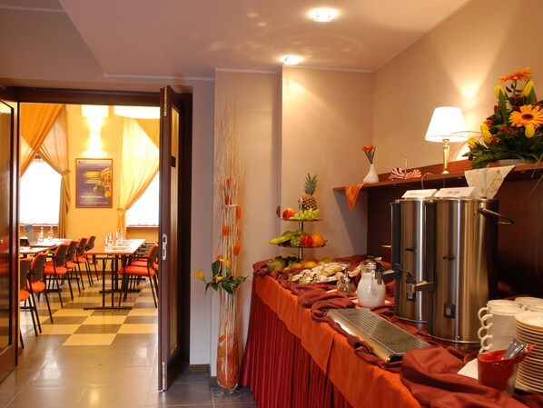 A hotel breakfast area with a buffet setup, including a variety of fruits and pastries, a coffee station, and a seating area with tables and chairs. - EA Hotel Downtown (Prague)