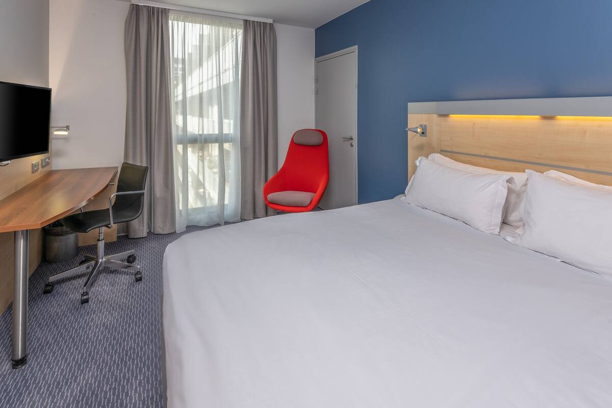Una habitación de hotel con una cama, un escritorio con una silla, un televisor y una silla roja.