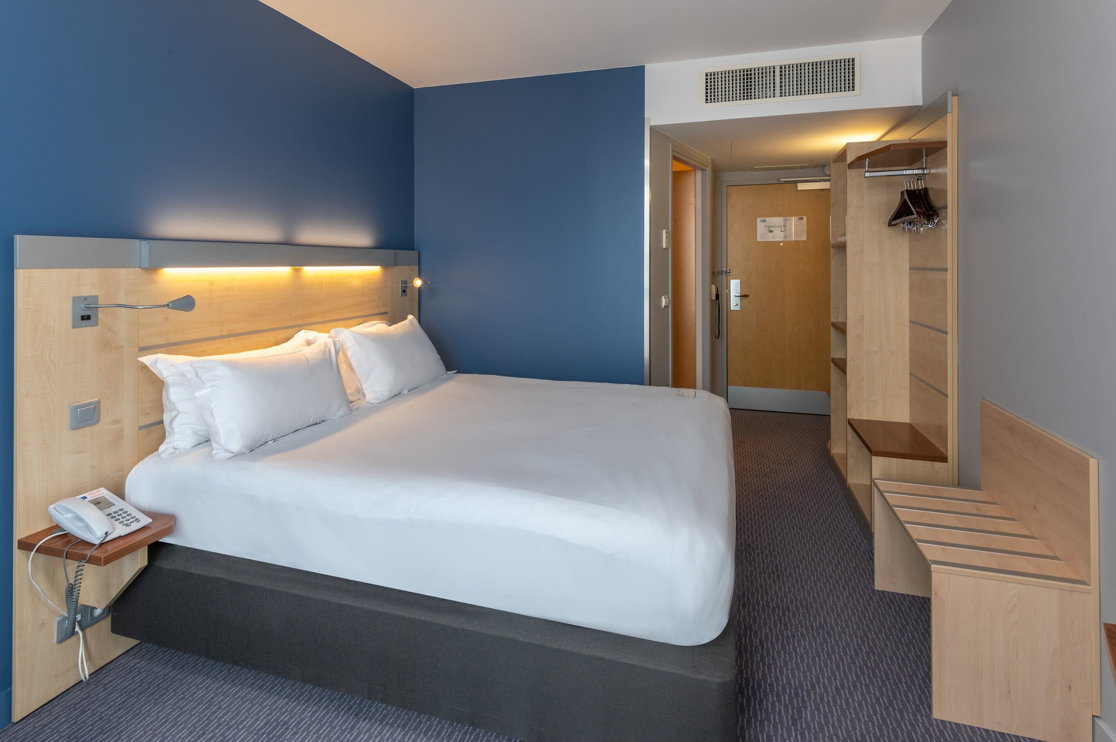 A hotel room with a bed, a bedside phone, and a wooden headboard.