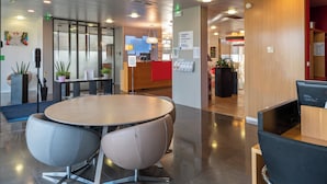 A modern hotel lobby with a round table and chairs, a reception desk, and a dining area.