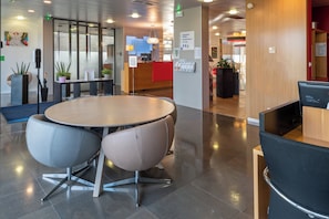A modern hotel lobby with a round table and chairs, a reception desk, and a dining area. - Holiday Inn Express Saint-Nazaire by IHG (Saint-Nazaire)