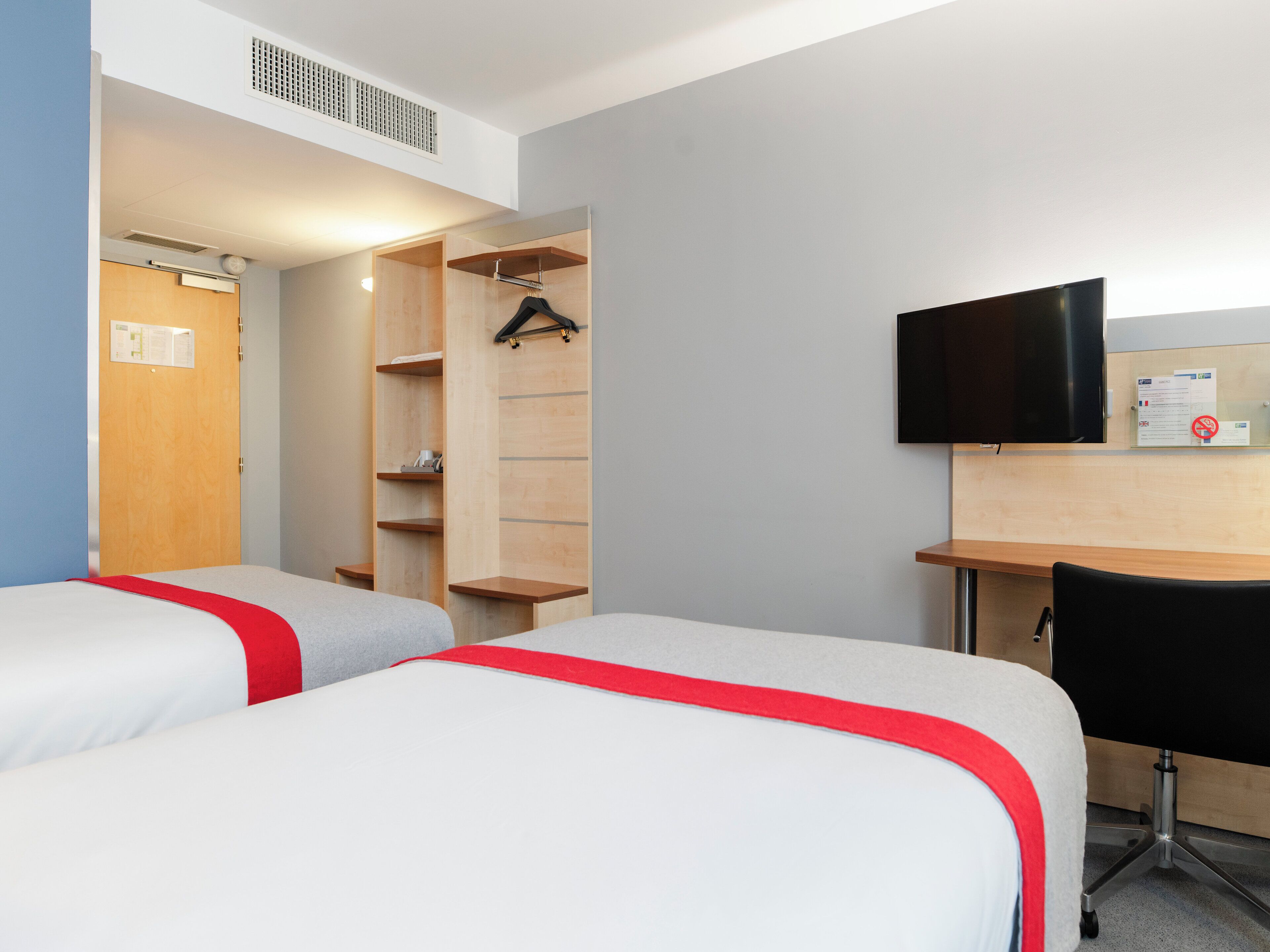 Una habitación de hotel con dos camas, un escritorio, un televisor y un armario.