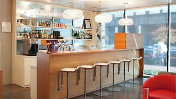 Una zona de bar con mostrador de madera, varios taburetes y una variedad de botellas y vasos.