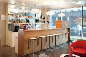 Una zona de bar con mostrador de madera, varios taburetes y una variedad de botellas y vasos.