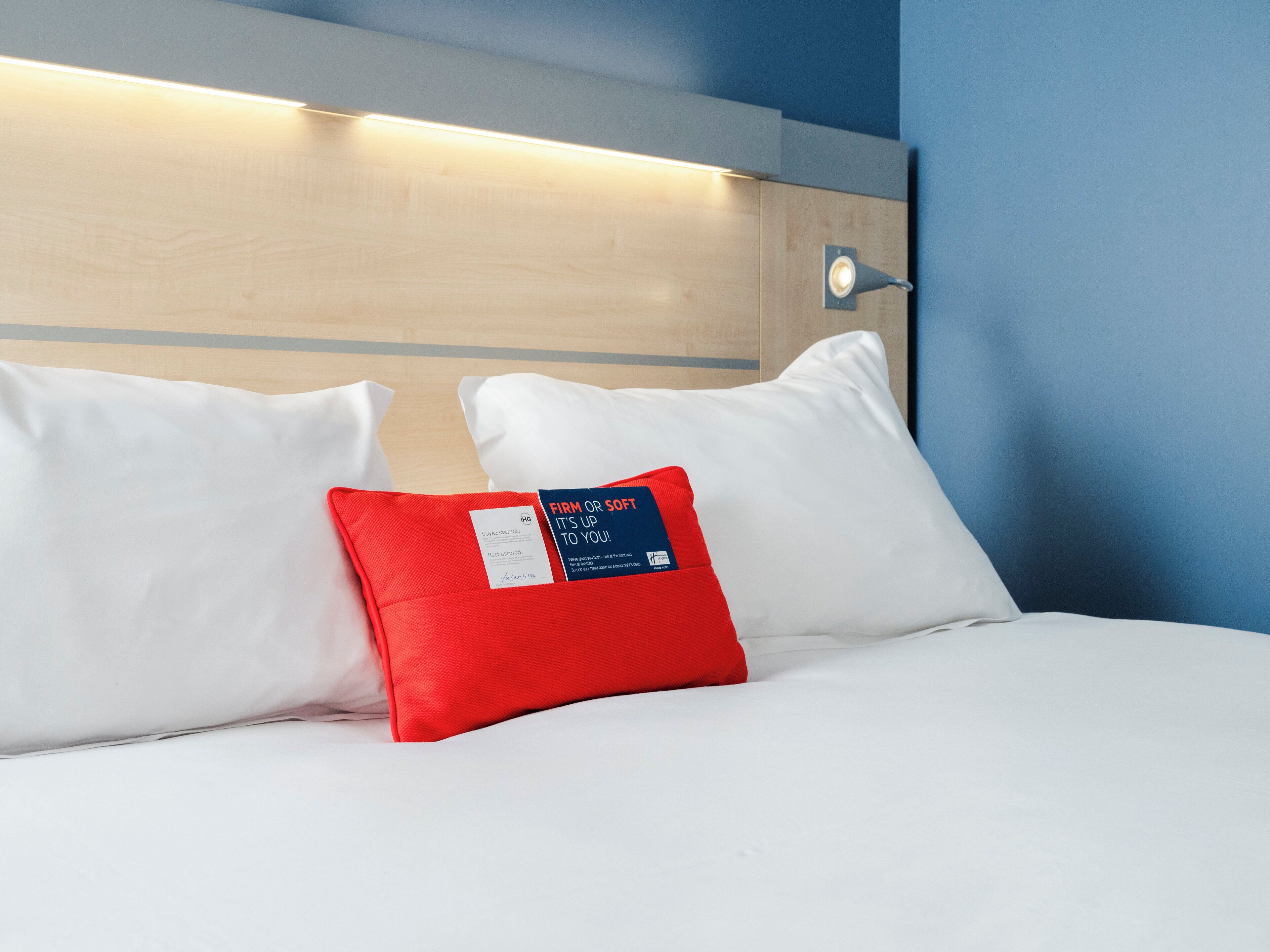 A hotel room with a wooden headboard, white bedding, and a red pillow with a tag.