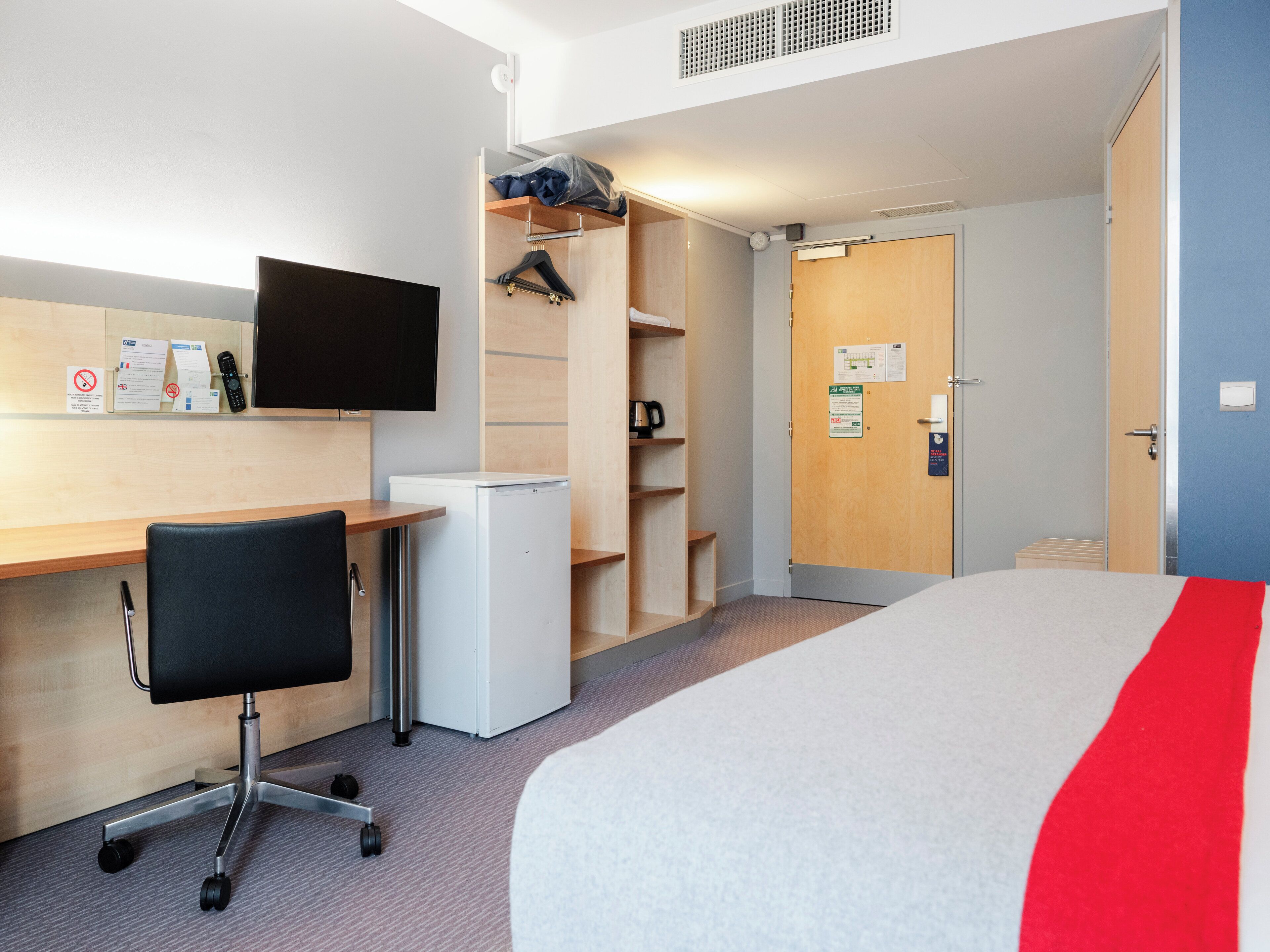 A hotel room with a bed, desk, chair, and a television.