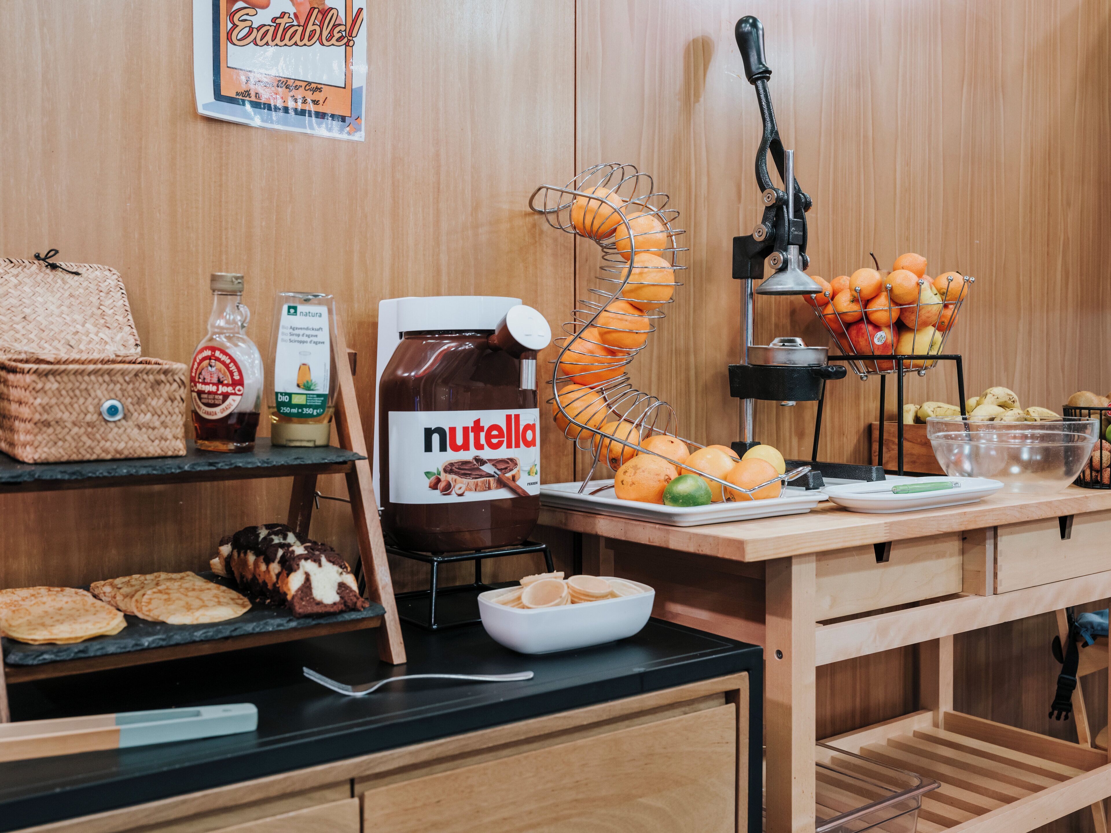 Eine Küchenarbeitsplatte mit einem Nutella-Glas, einem Obstkorb und einer Ahornsirupflasche.