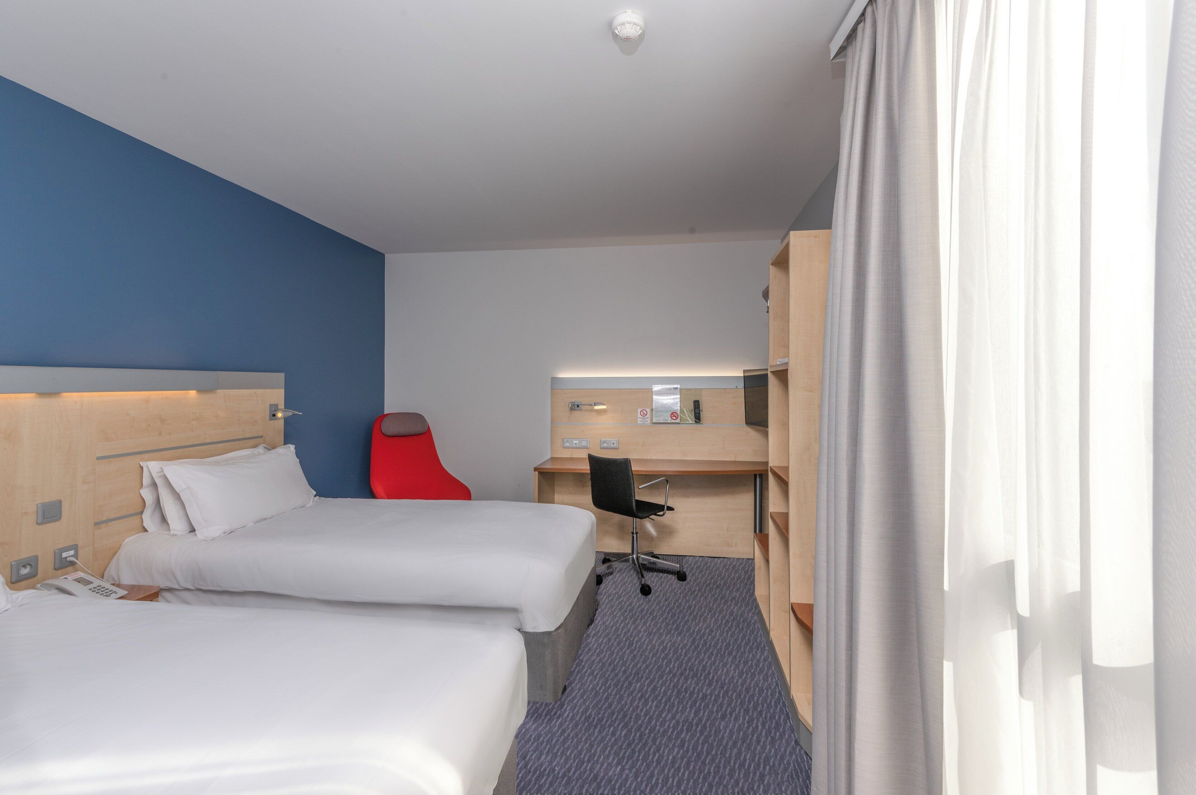 Une chambre d’hôtel avec deux lits, un bureau, une chaise, un téléphone et un miroir.