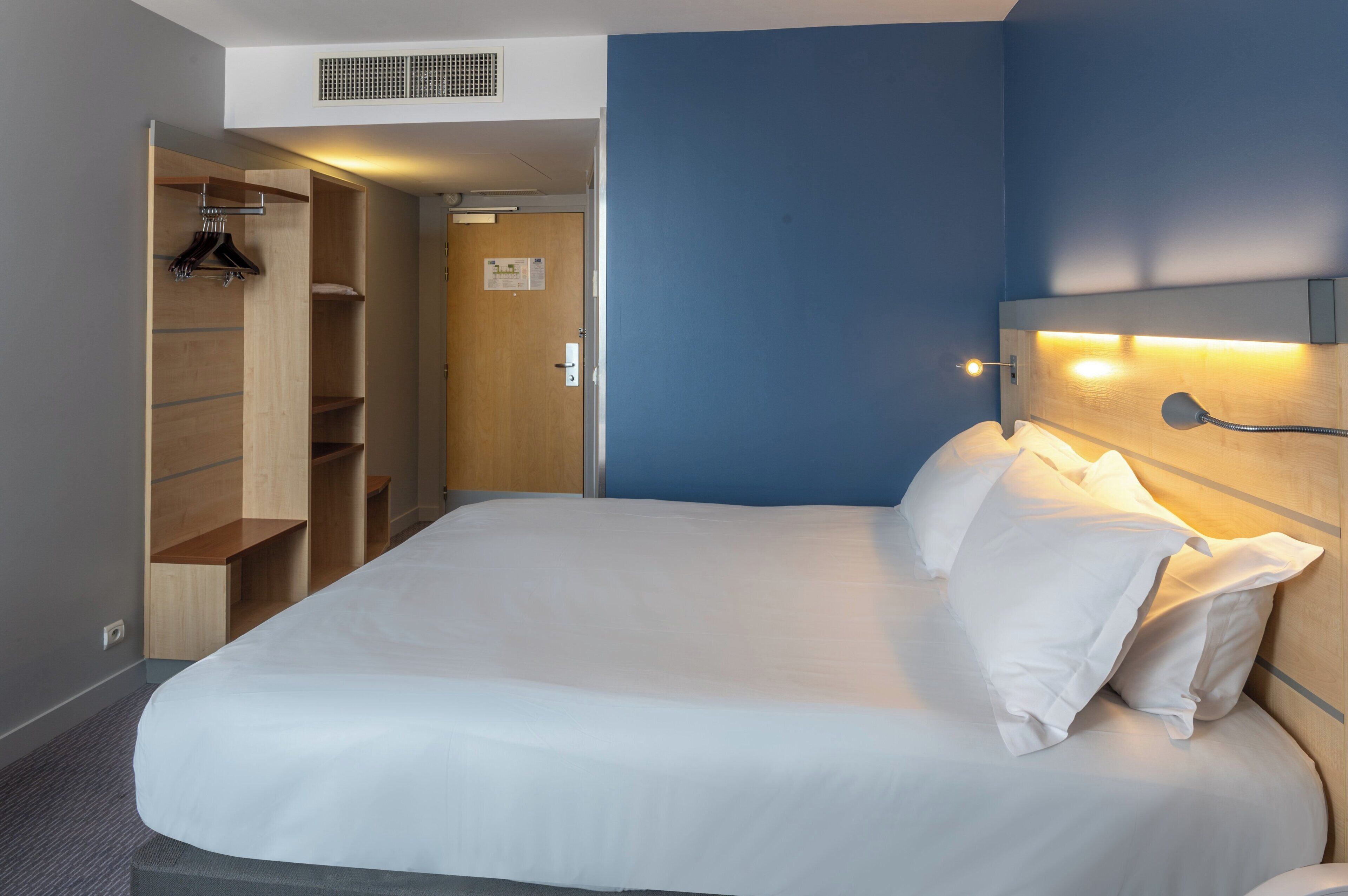 Una camera d'albergo con un letto grande, un armadio in legno e una parete decorata in blu.