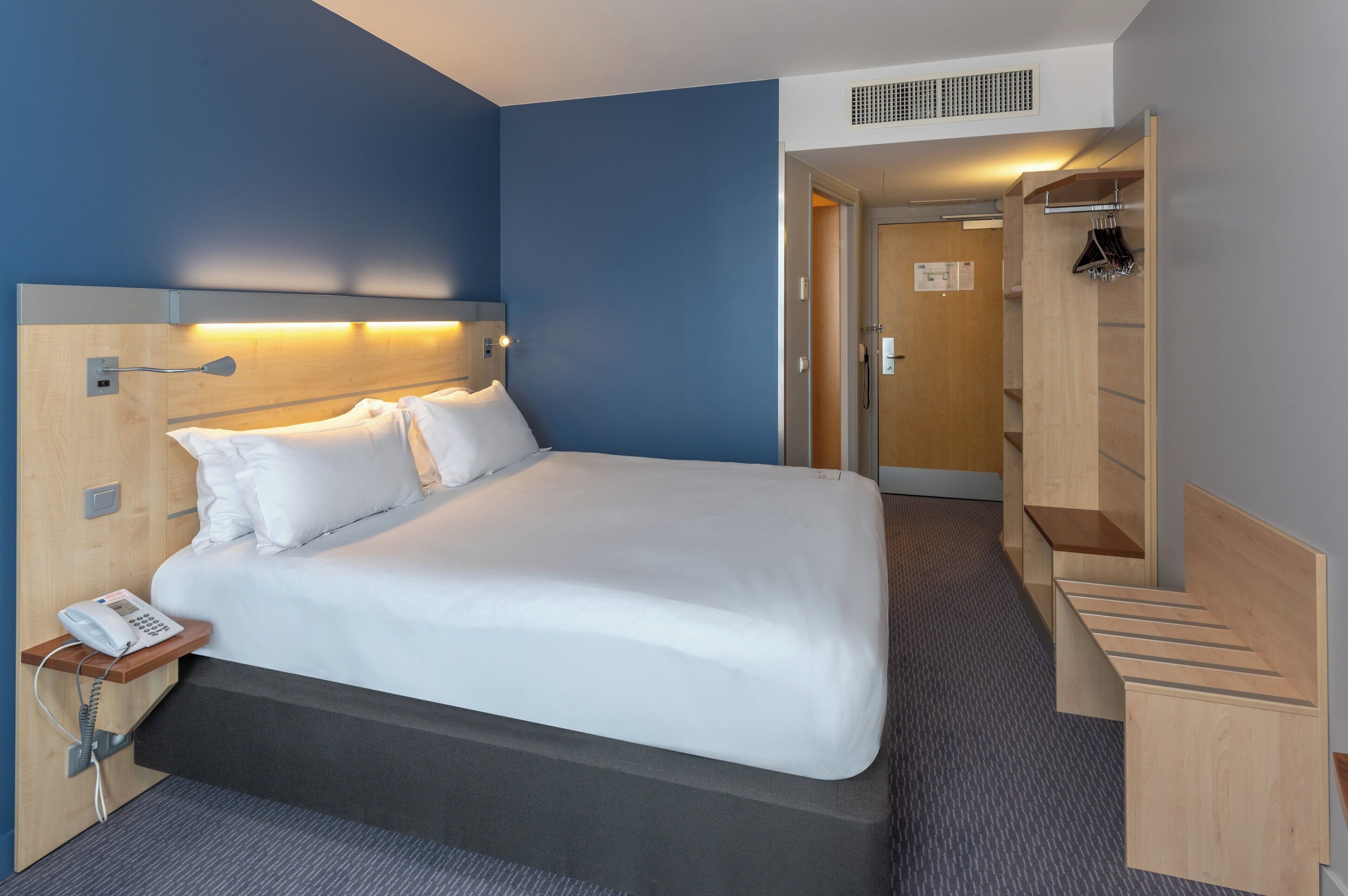 A hotel room with a bed, bedside phone, and a wooden headboard.