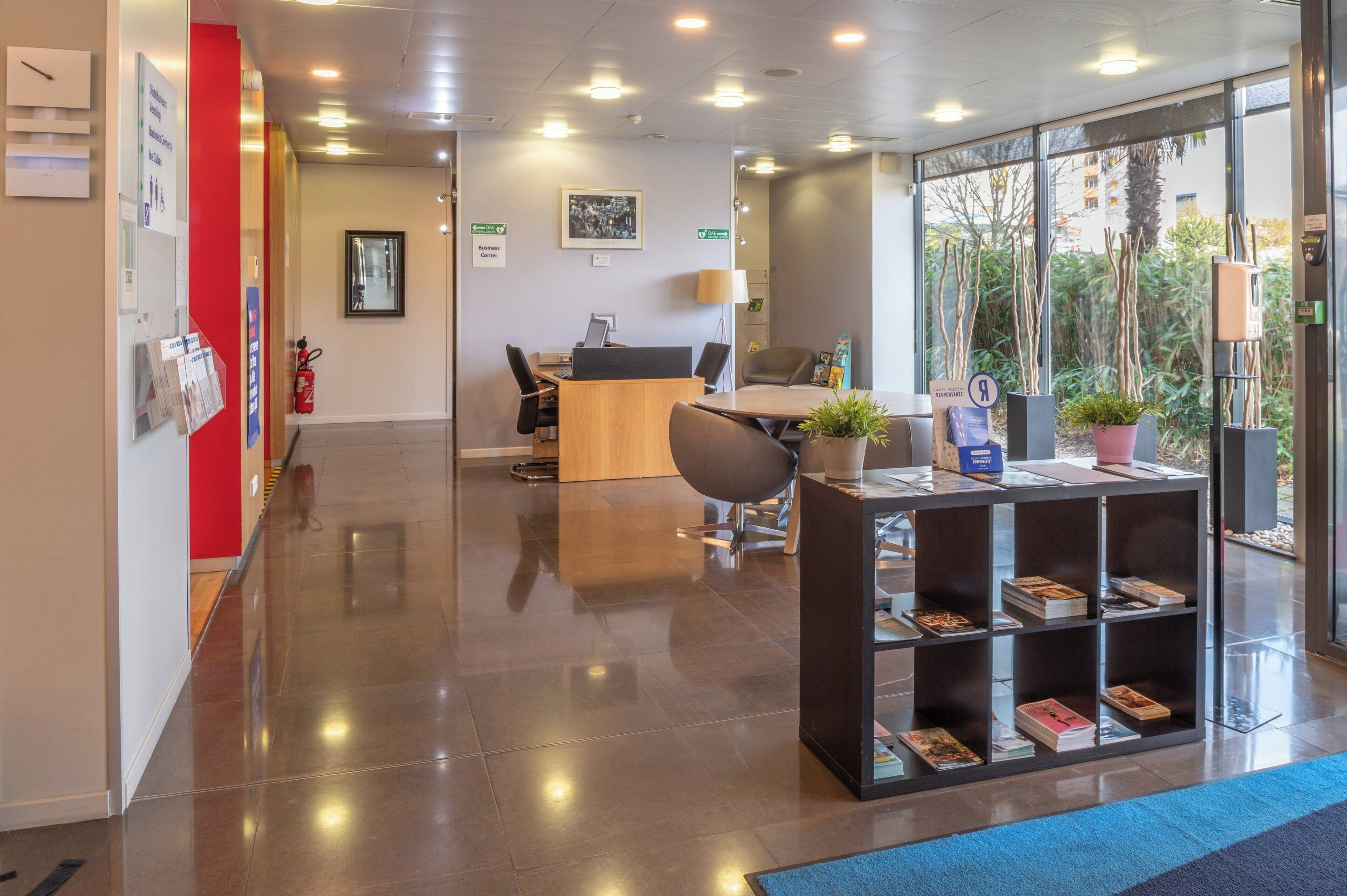 A modern reception area with a desk, chairs, a fire extinguisher, and a bookshelf with magazines.