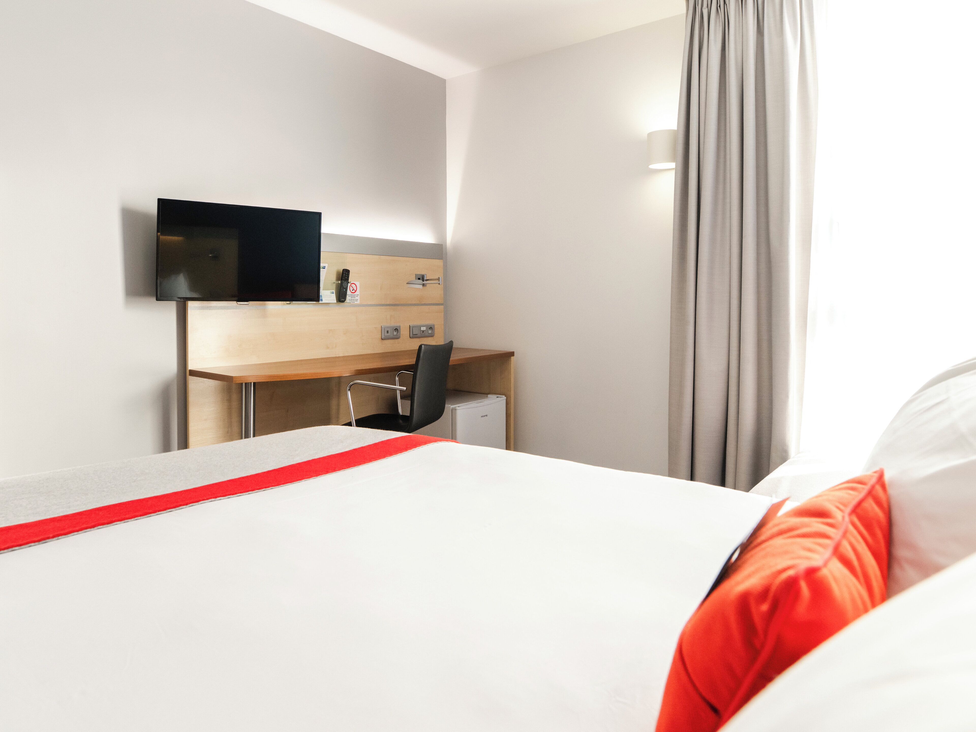 A hotel room with a bed, a desk, a chair, a television, and a window with curtains.