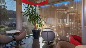 A modern indoor space with a large potted plant, seating arrangements, and a view through a window.