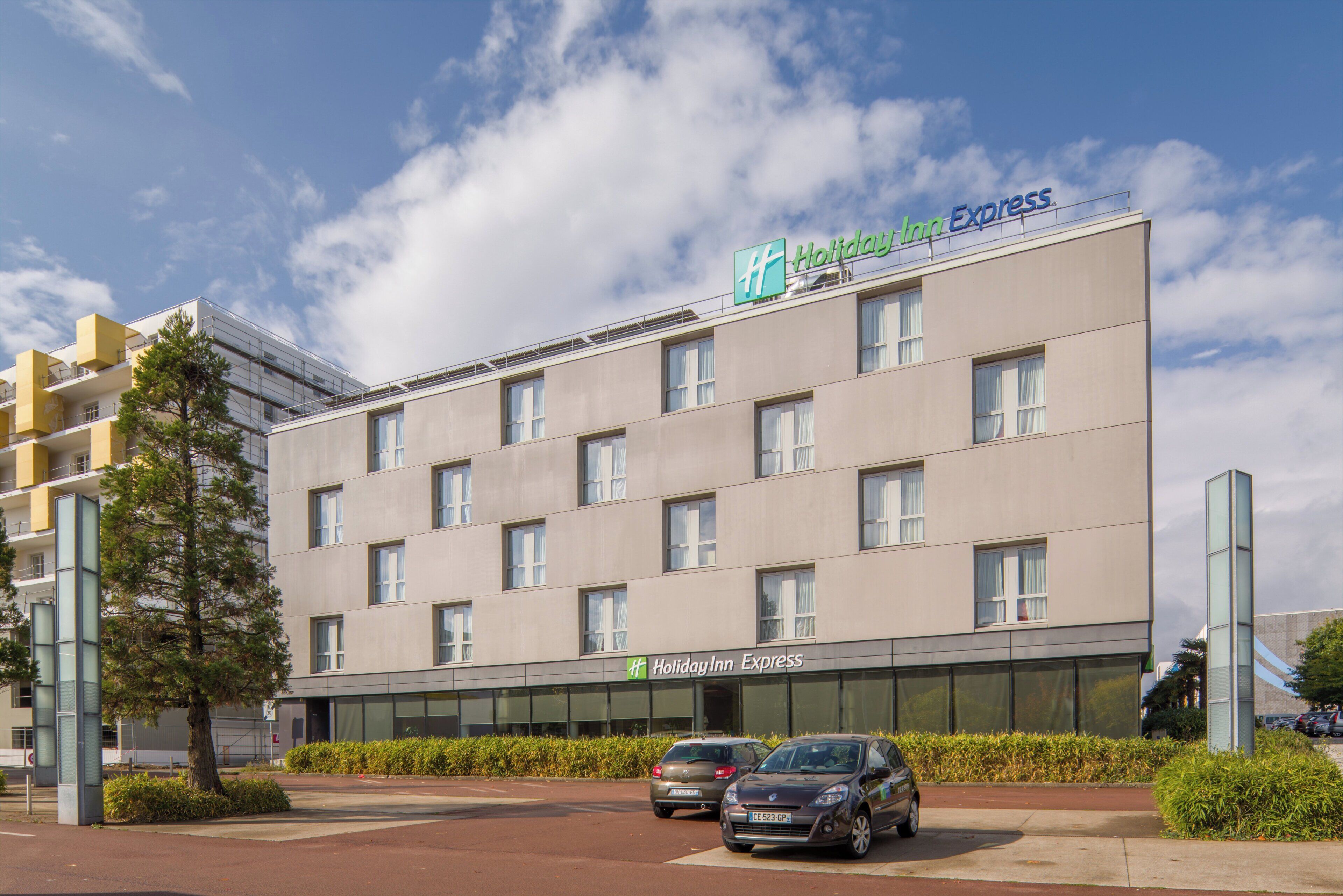 Een Holiday Inn Express gebouw met een moderne gevel, meerdere ramen en een parkeerplaats met auto's.
