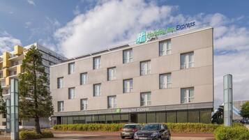 Un bâtiment de l’hôtel Holiday Inn Express, doté d’une façade moderne, de nombreuses fenêtres et d’un parking avec des voitures.