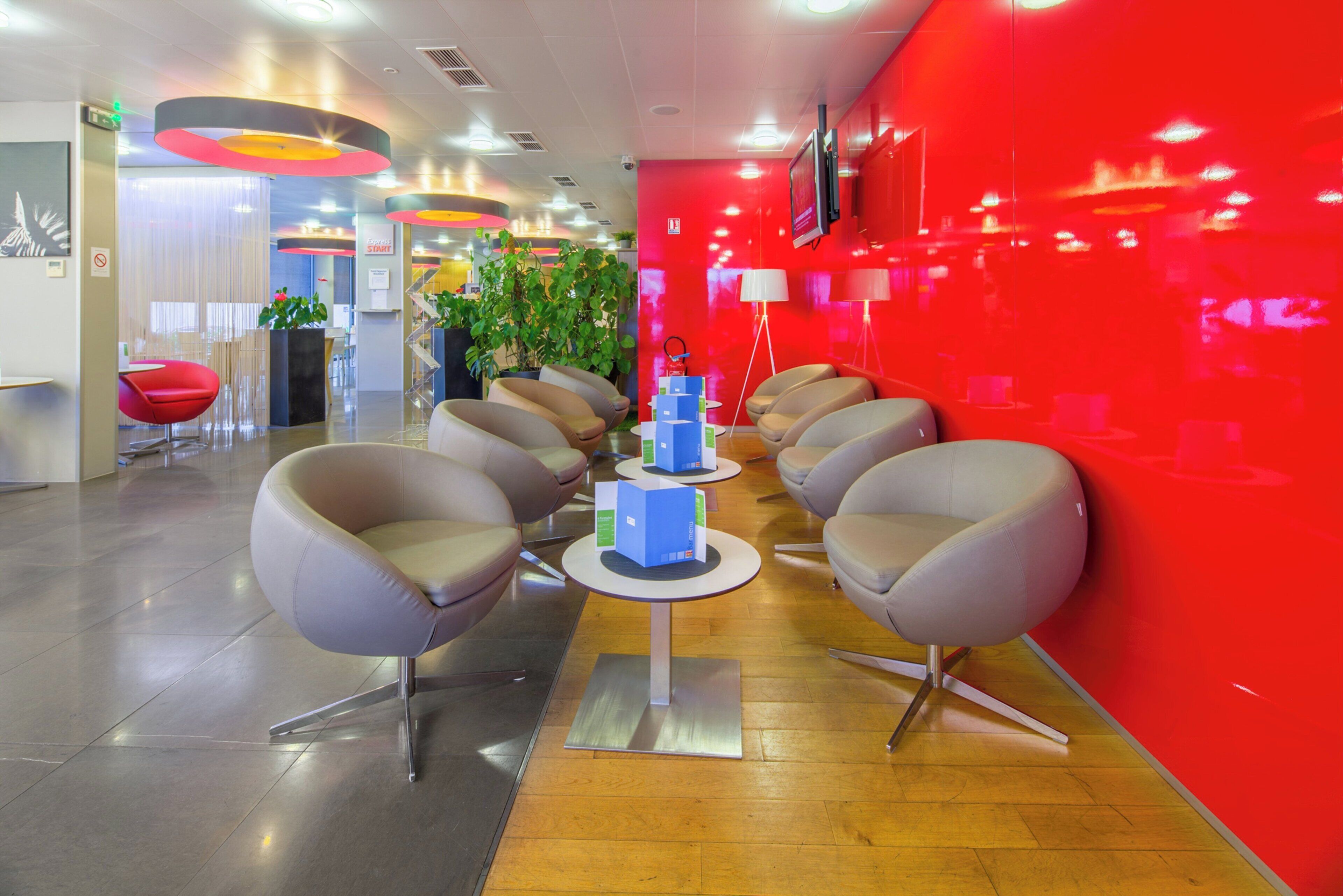 A modern waiting area with a red accent wall, multiple seating options, and a central table with informational brochures.