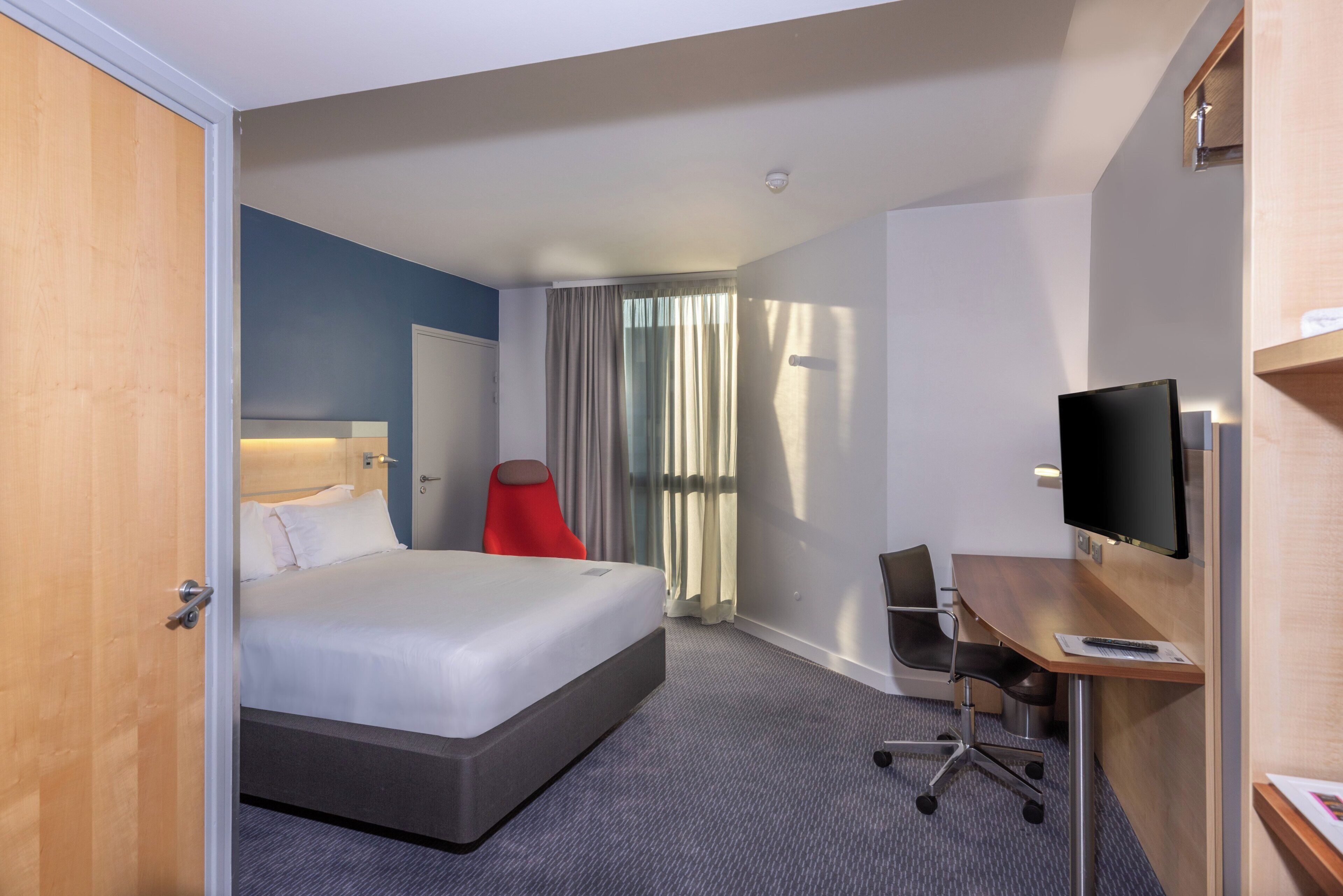 A hotel room with a bed, a desk, a chair, a television, and a window with curtains.