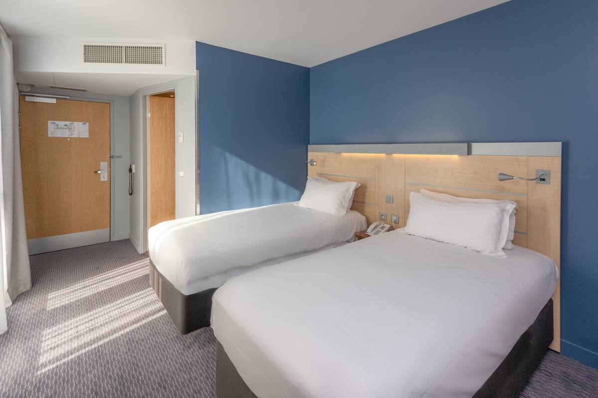Habitación de hotel con dos camas, una puerta de madera, un teléfono y una lámpara en la pared.