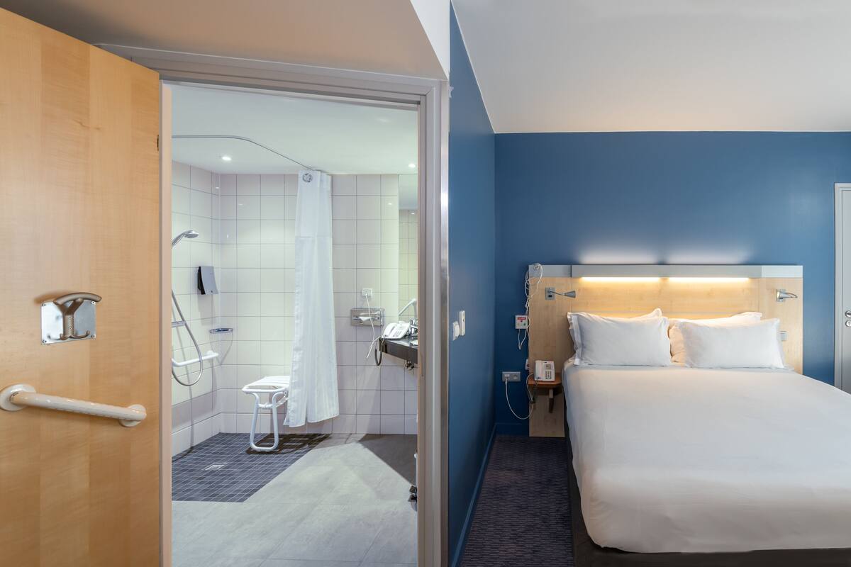 Habitación de hotel con cama, mesita de noche y baño visible a través de una puerta abierta.