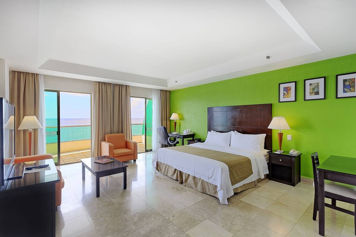 A hotel room with a bed, a desk, a chair, a table, and a view of the ocean.