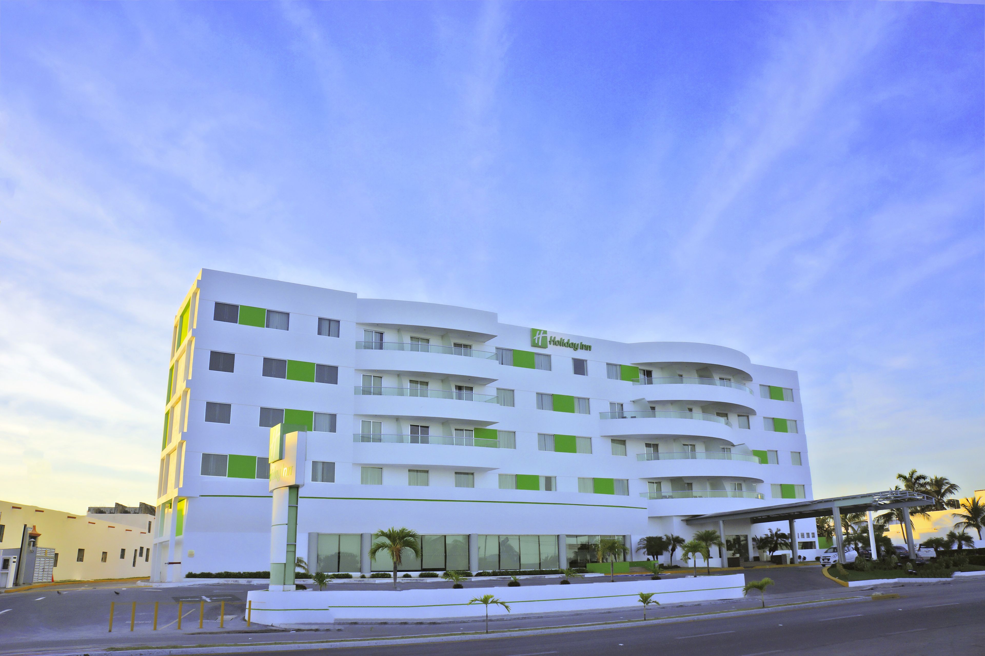 Un hôtel Holiday Inn moderne, avec une façade blanche et des touches de vert, doté d’une entrée couverte et d’un espace de stationnement.