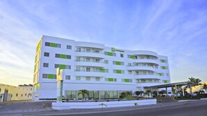 Un hotel moderno Holiday Inn con fachada blanca y detalles verdes, que cuenta con una entrada cubierta y un área de estacionamiento.
