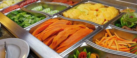 A buffet with various food items including fruits, vegetables, and meats.