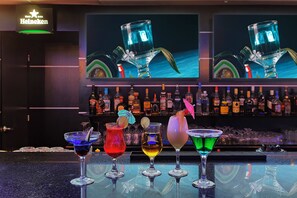 Un bar con una variedad de bebidas coloridas y un letrero de Heineken al fondo.