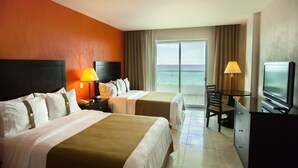 Habitación de hotel con dos camas, televisión, escritorio y vista al océano.