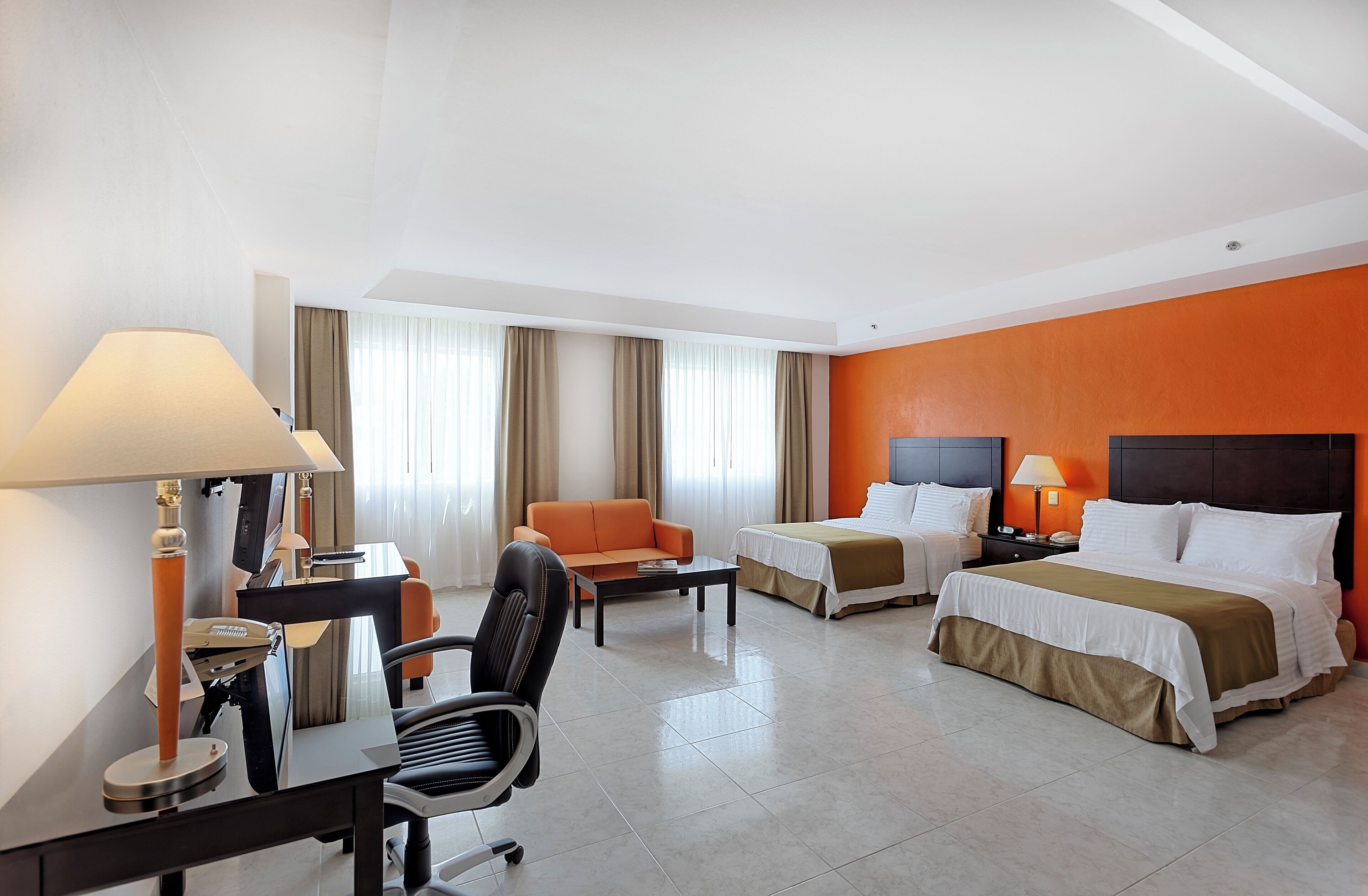 Una habitación de hotel con dos camas, un escritorio con silla, un sofá y una lámpara.