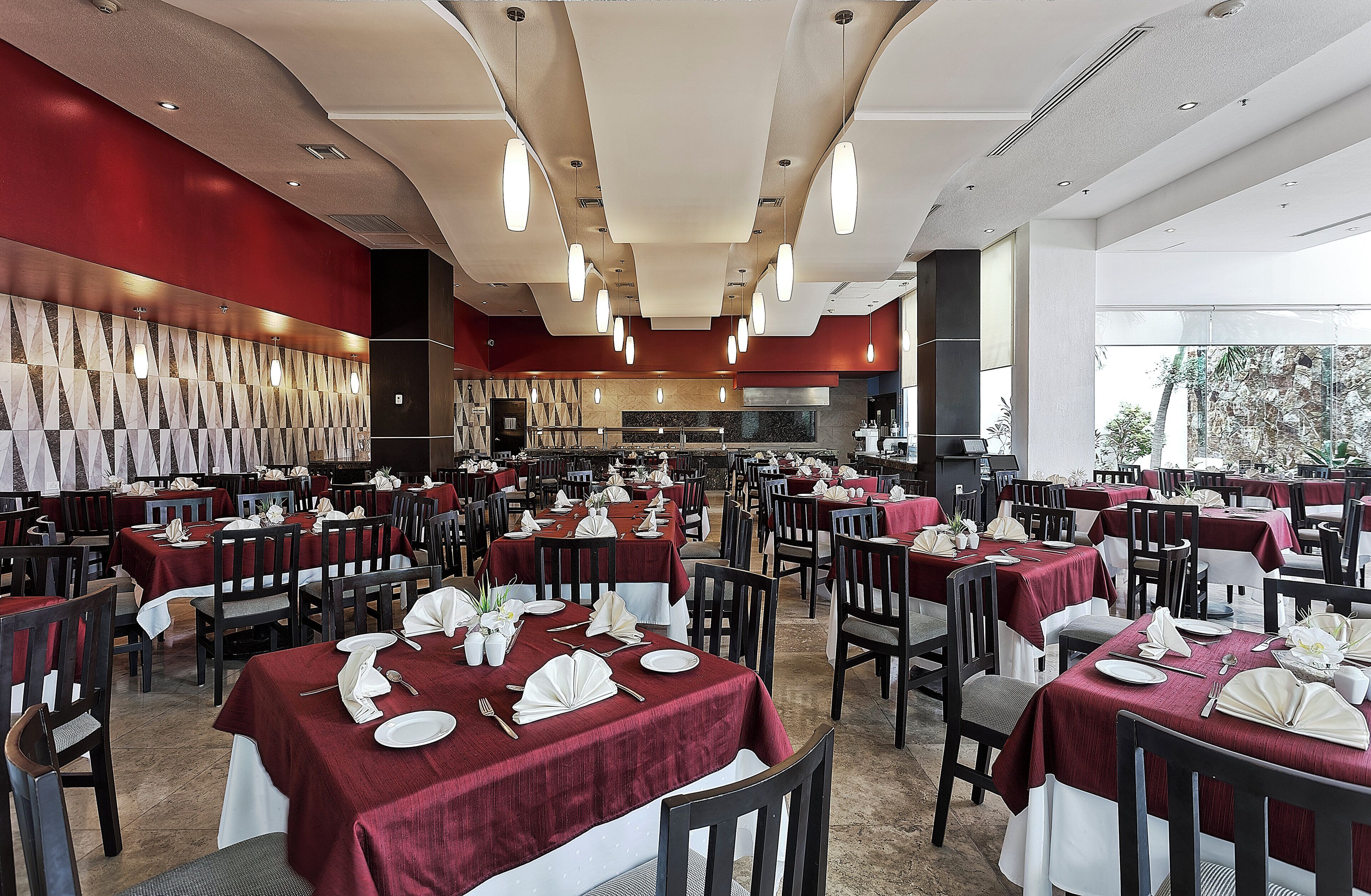 Un'ampia sala da pranzo con diversi tavoli apparecchiati, una cucina spaziosa sullo sfondo e vista sull'esterno attraverso ampie finestre.