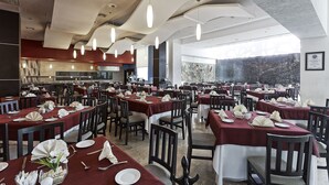 Un comedor amplio con varias mesas dispuestas para el servicio, una cocina al fondo y vistas al exterior.