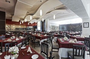Un comedor amplio con varias mesas dispuestas para el servicio, una cocina al fondo y vistas al exterior.