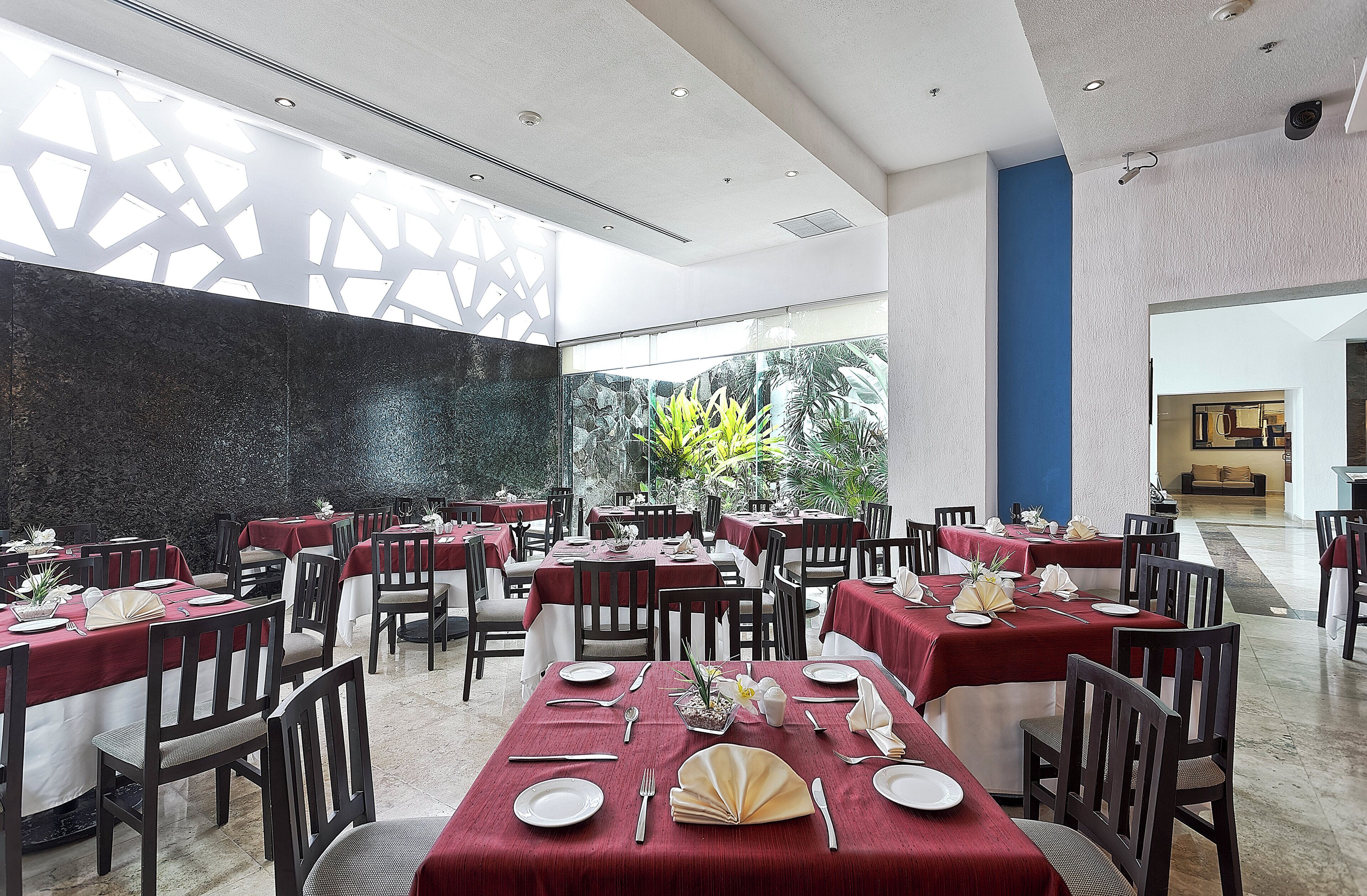 A restaurant with multiple tables set for dining, featuring a modern interior with a mix of natural and artificial lighting.