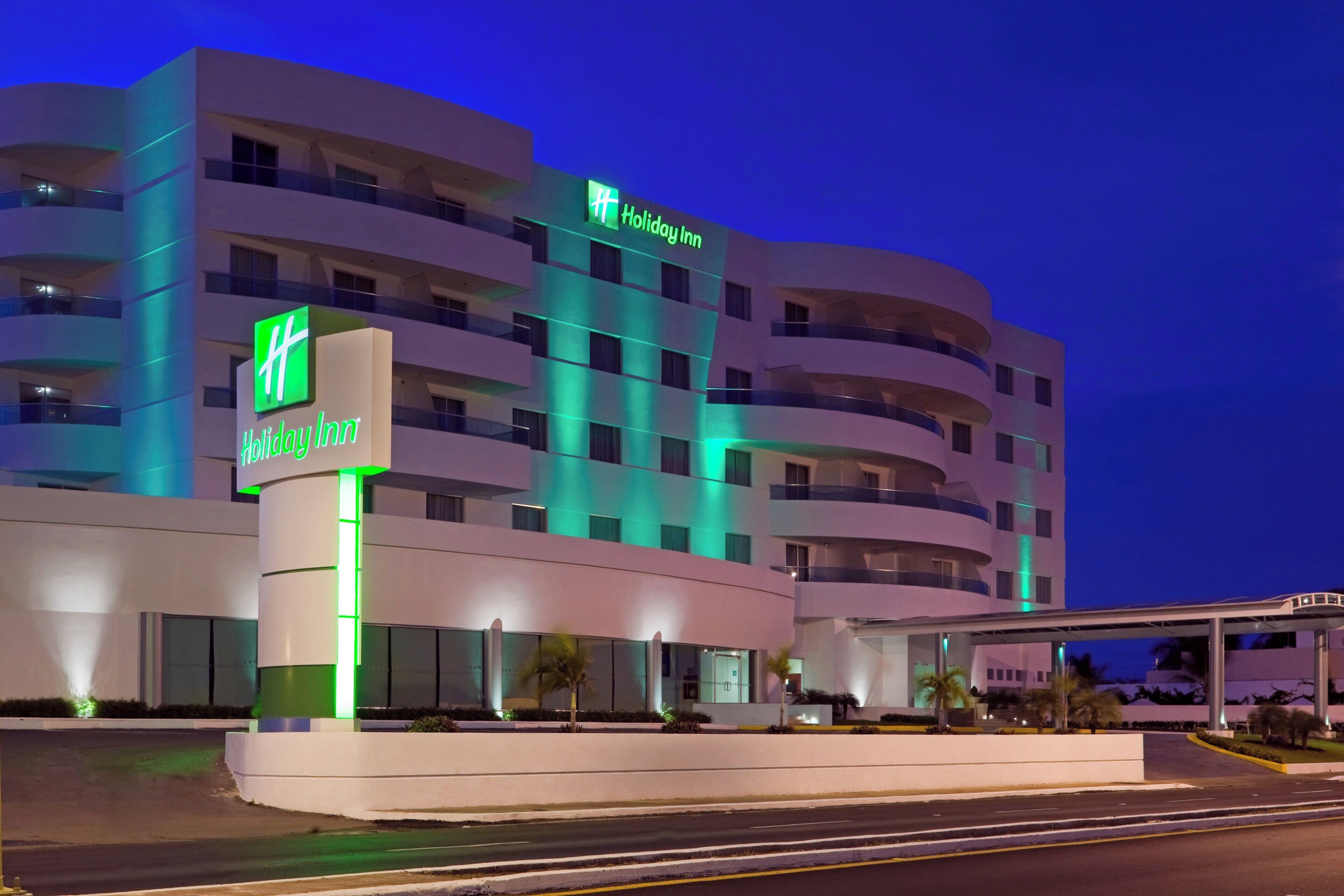 A Holiday Inn hotel with a modern design, featuring multiple balconies and a prominent green sign.